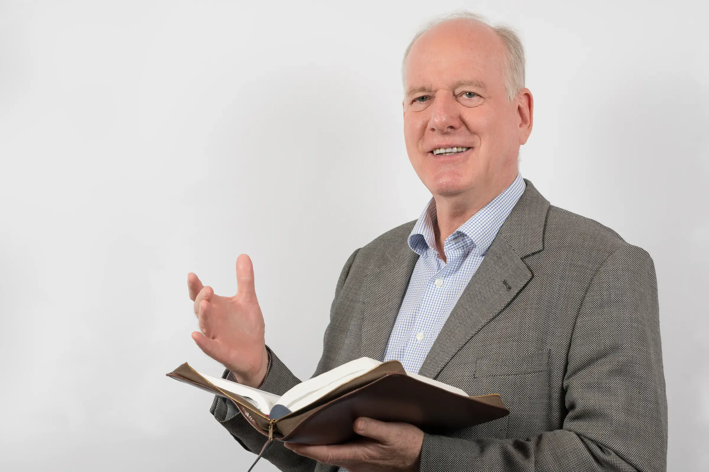 Portrait von einem ältere Mann in einem grauen Anzug, der in der linken Hand eine Bibel hält und die rechte leicht erhoben hat.