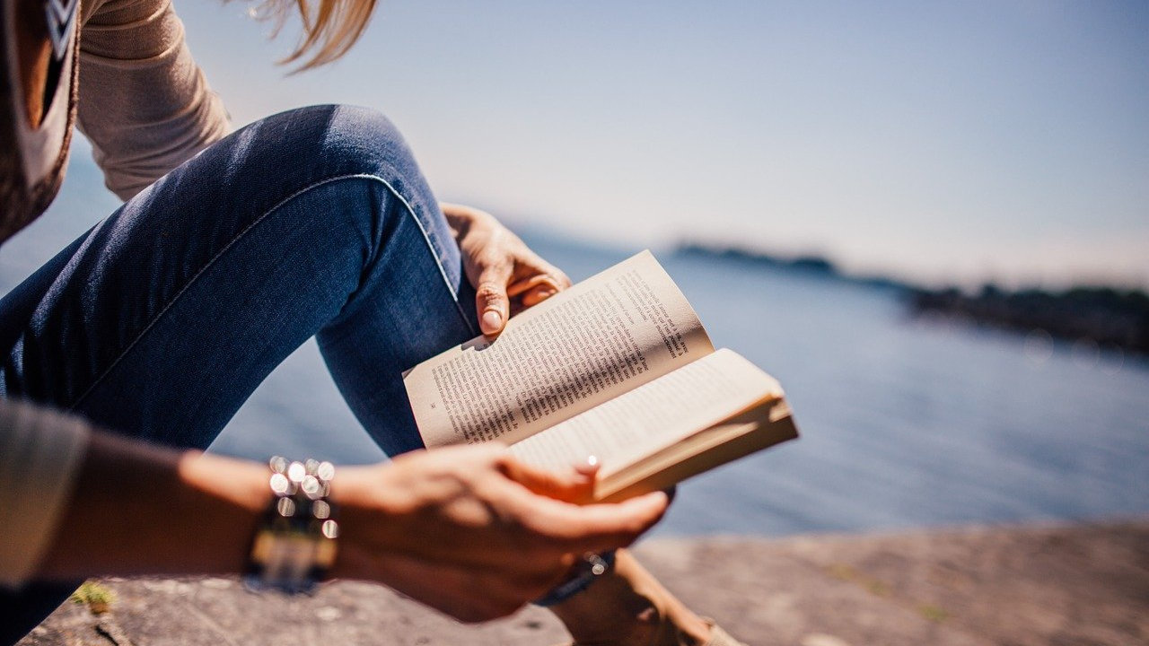 Symbolbild: Frau liest ein Buch, im Hintergrund Meer